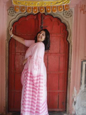 Gulabi Dhoop saree in blush pink cotton with floral motifs in pink shades, striped pallu, tassels, and matching blouse piece.