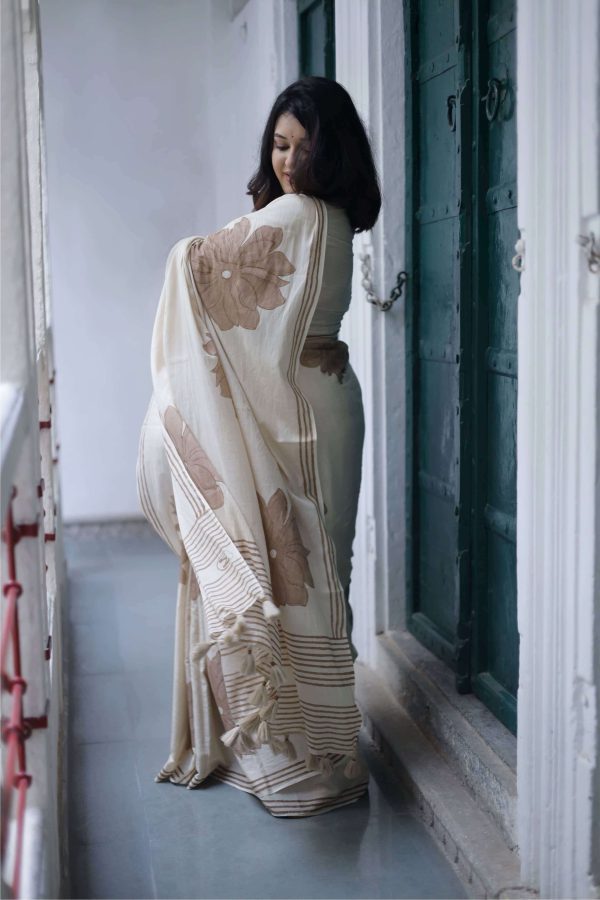 Komal cotton saree in almond beige with hand-block printed brown floral motifs, dark brown border, tassels on the pallu, and matching blouse piece.