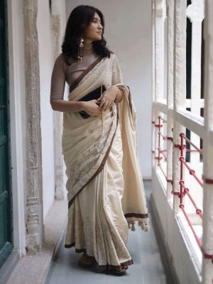 Saumya beige cotton saree with dark brown floral and bird hand-block motifs, dark brown border, plain body, tassels, and matching blouse fabric.