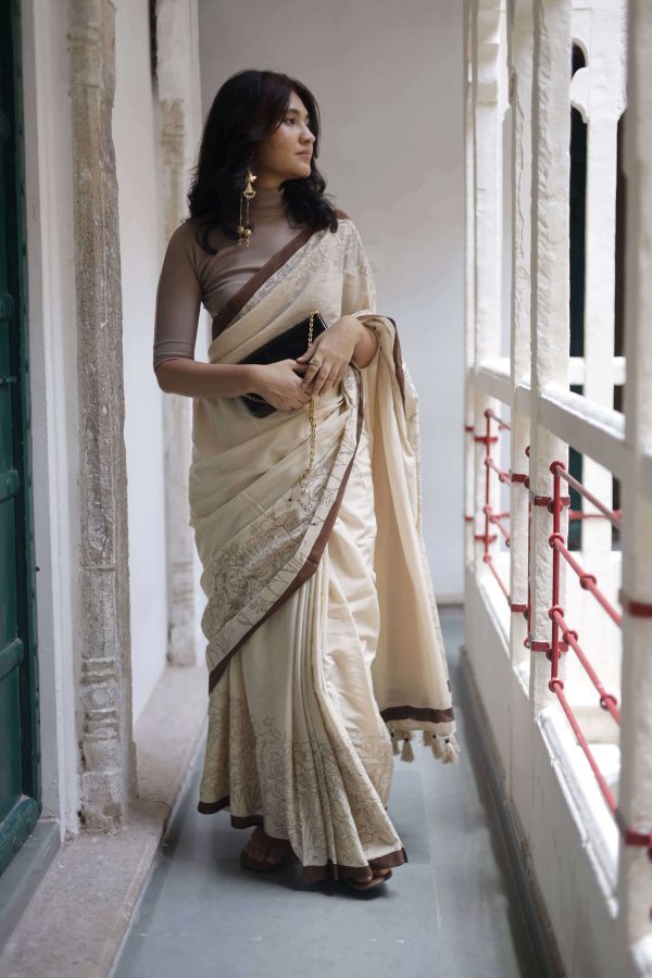Saumya beige cotton saree with dark brown floral and bird hand-block motifs, dark brown border, plain body, tassels, and matching blouse fabric.